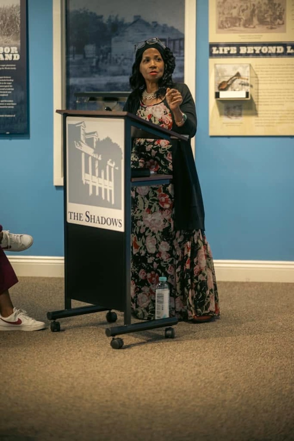 Ruth Foote speaking at a podium at The Shadows-on-the-Teche, in front of exhibit panels on slavery and desegregation